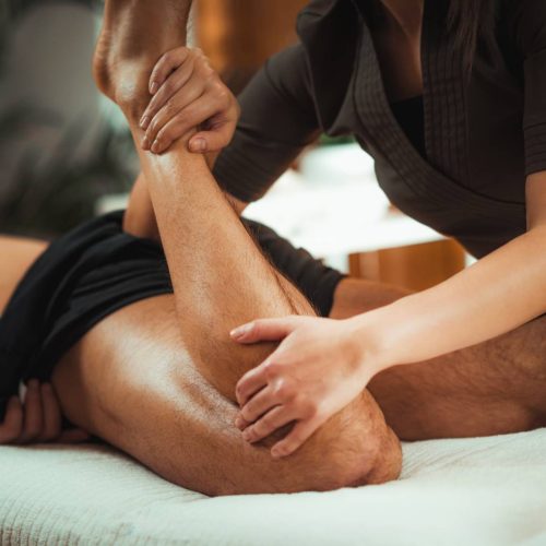 Physiotherapist massaging male patient with injured leg muscle. Sports injury treatment.